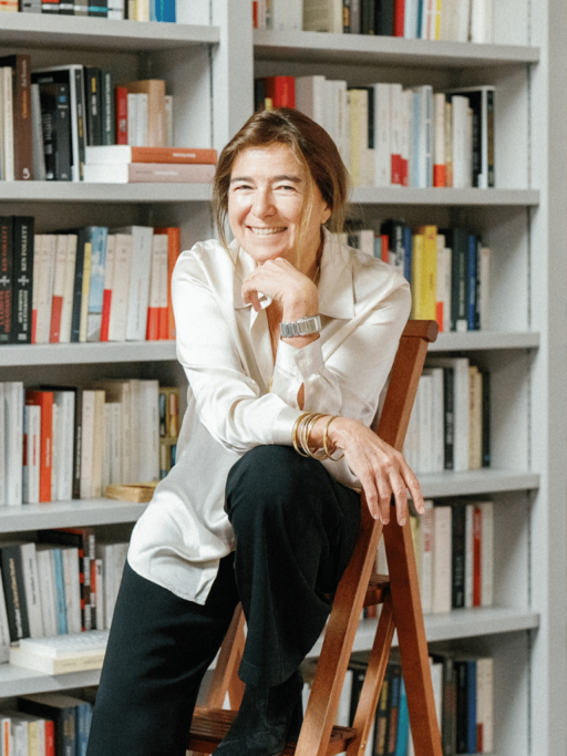 Valérie Gans, assise sur une échelle devant une grande bibliothèque